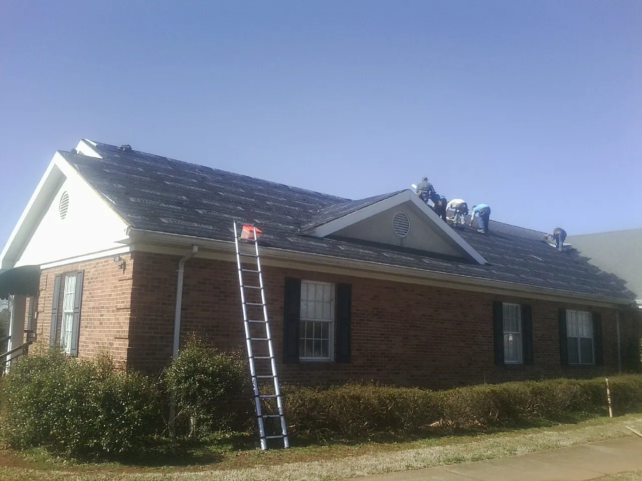 Crew tearing shingles off a brick ranch roof with a ladder set — Metal Roof Repair work by our crew in Kerhonkson