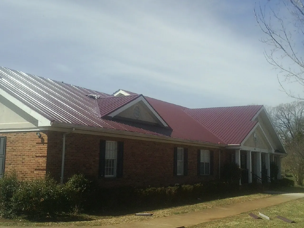 Red metal roof with gabled entries on a long brick building, from a Hail Damage Roof Repair job in Kerhonkson