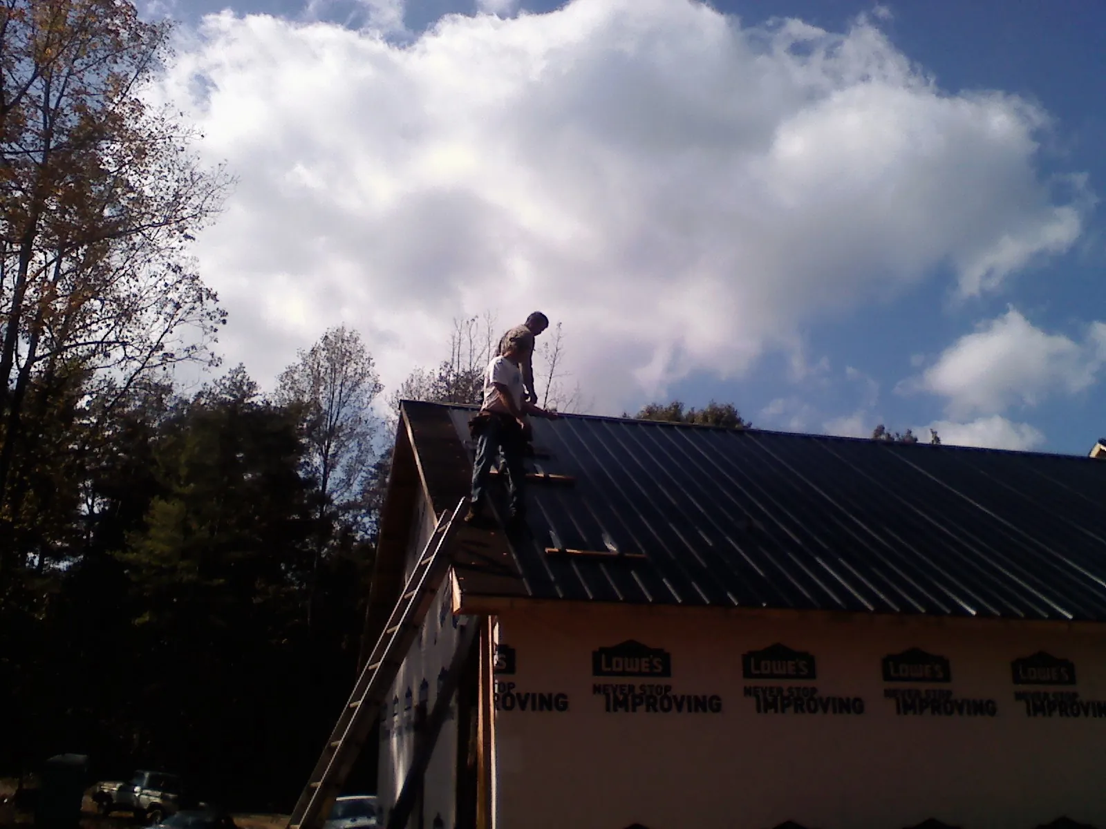 Roofer fastening dark metal panels high against a cloudy sky, from a Roof Inspection job in Kerhonkson