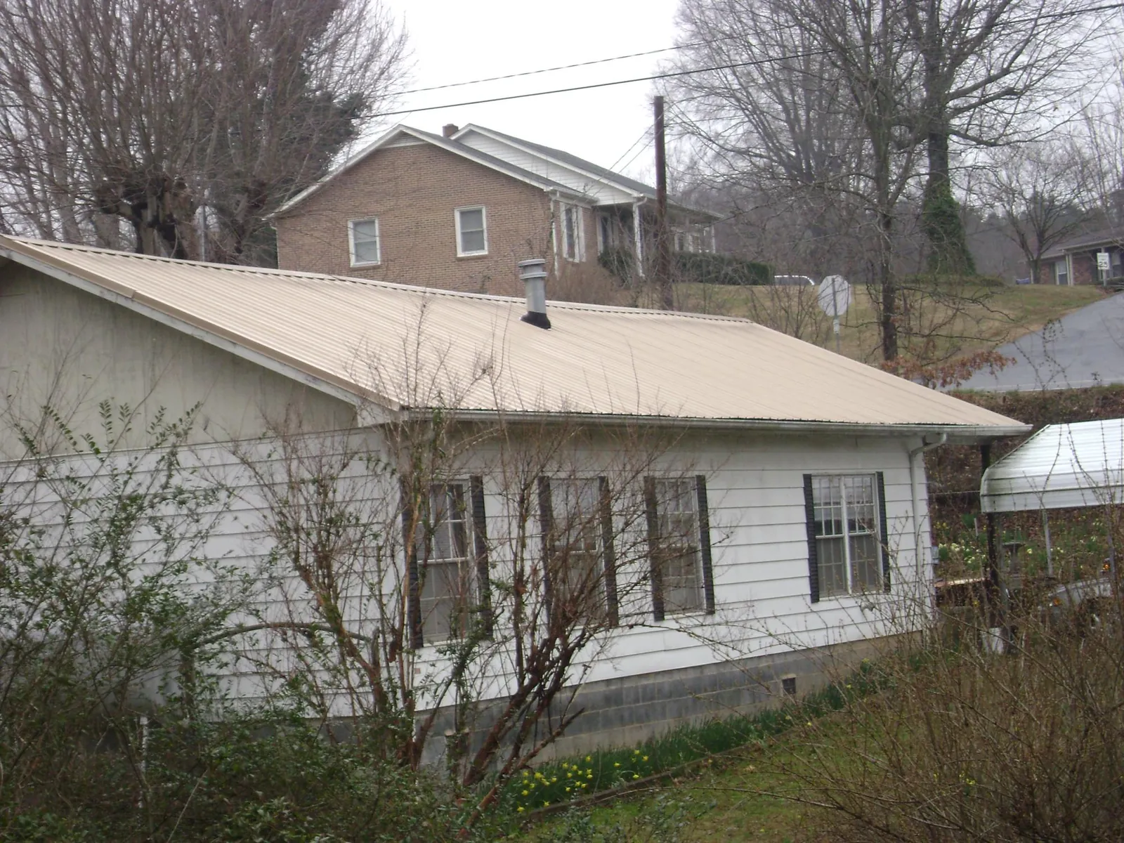 Tan metal roof on a white sided house set into a hillside — Commercial Roofing by Roofing Brothers in Kerhonkson